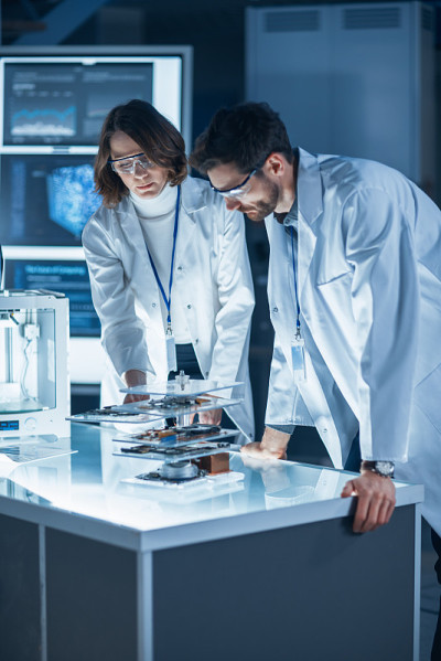 由身穿白大褂的工业科学家和工程师组成的多样化国际团队在研究实验室从事重型机械设计工作。专业人士使用3