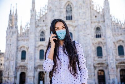 一名亚洲女性戴着医用口罩在米兰大教堂使用智能手机