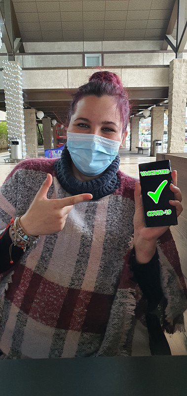 戴着口罩的快乐白种人女性，在智能手机上展示了国际疫苗接种证书。关闭了。数字健康疫苗护照