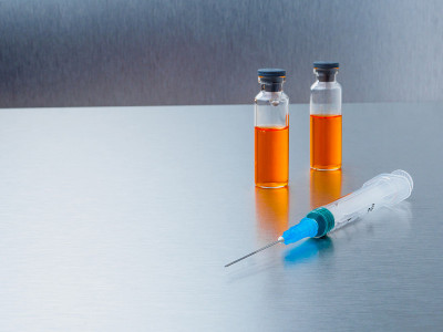 注射用注射器和两支冠状病毒疫苗安瓿，背景为银色铝。