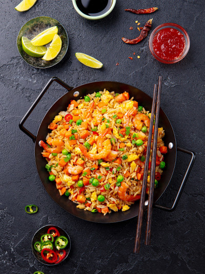 用黑色铁锅将米饭、蔬菜和虾炒熟。板岩的背景。前视图。