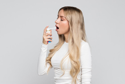 心烦意乱的年轻金发女人用喷雾治疗喉咙痛。喉咙痛，吞咽痛