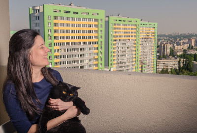 一个带着黑猫的女孩从阳台看向一座新楼