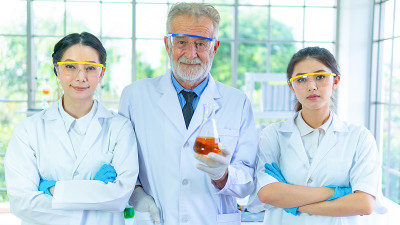 科学家们聚在白袍下凝神站着。与背景室内白色实验室。