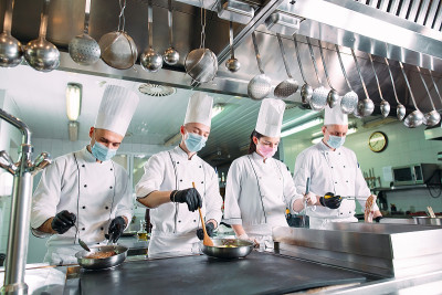 厨师戴着防护口罩和手套在餐厅或酒店的厨房里准备食物。