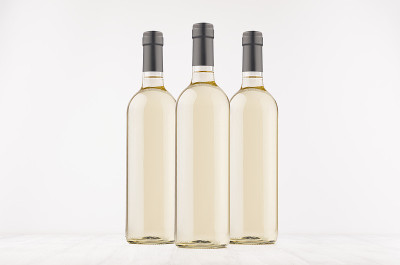 三个透明的葡萄酒瓶和白葡萄酒在白色木板上，模拟。