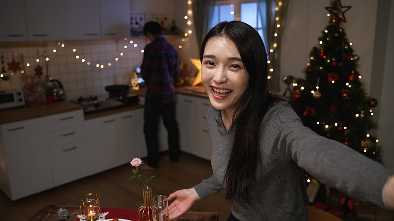 两对有趣的夫妇在舒适的厨房里准备圣诞晚餐。年轻的韩国女孩拿着相机面对镜头，打电话给男朋友在这里加入视