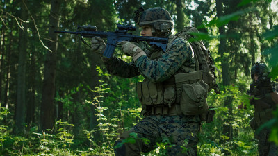 一队全副武装的迷彩服士兵正在执行一项侦察军事任务，瞄准步枪。他们在密林中列队行进。