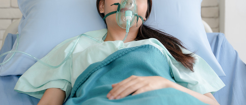 亚洲妇女病人在医院的床上戴着氧气面罩
