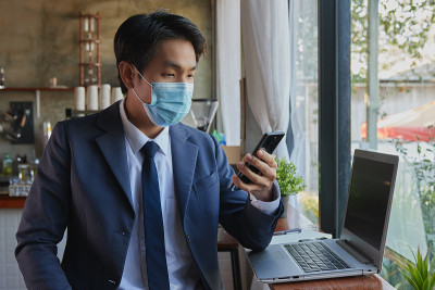 右前亚洲商人使用智能手机时戴口罩
