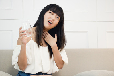 那位亚洲妇女咳嗽，喉咙痛。喉咙痛的原因包括流感和过敏。