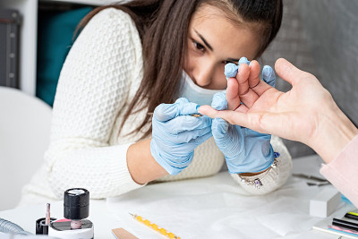 Manicure master in mask and gloves putting on gel 