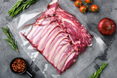 生法式羊排有机肉密封塑料包装，在灰色石头桌子背景，俯视图平铺