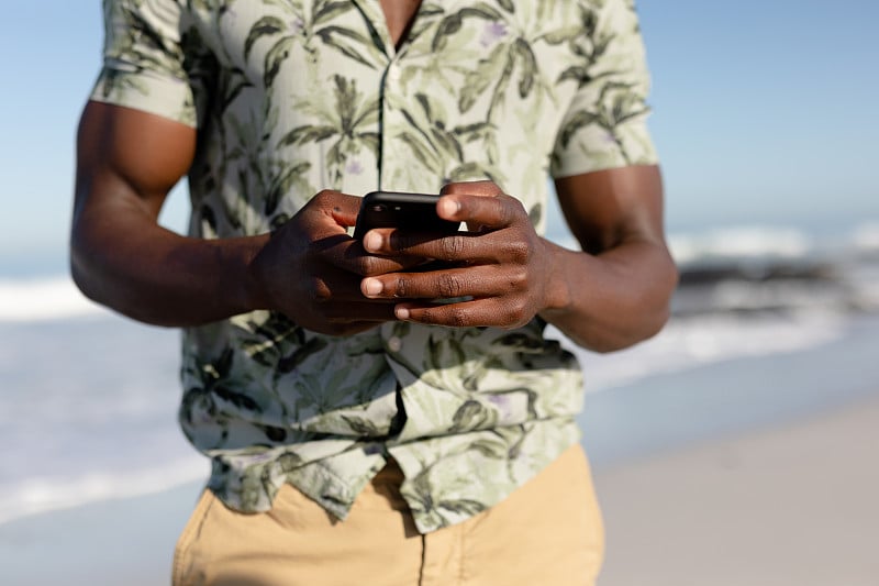 African american man using his phone on the beach