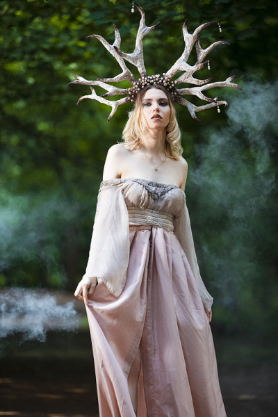 宁静的白人女孩的自然肖像在夏天的森林与灰色的烟雾后面与艺术鹿角在轻连衣裙摆姿势。垂直的形象定位