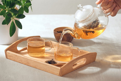 一只手从放在木托盘上的玻璃茶壶里倒茶