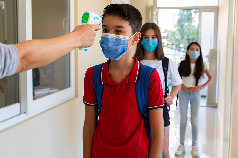 在学生返校期间，老师为戴口罩的学生检查体温