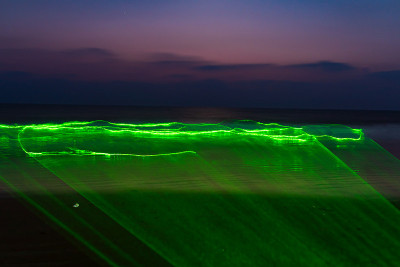 绿色激光在海滩上的海水上，夜间长曝光照片。