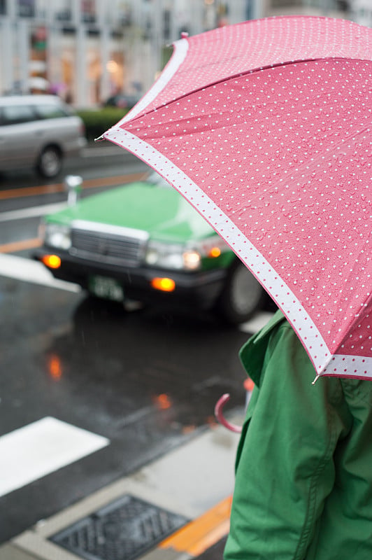 日本东京青山，一名身穿绿色外套、打着粉红色雨伞的女子