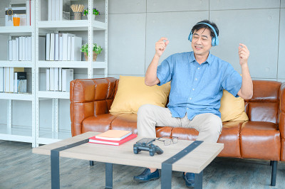 老人幸福坐在沙发上，用耳机听音乐在客厅放松