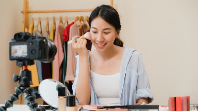 美妆博主坐在镜头前拍摄美妆视频。美女化妆点评化妆教程由互联网向社交网络直播。
