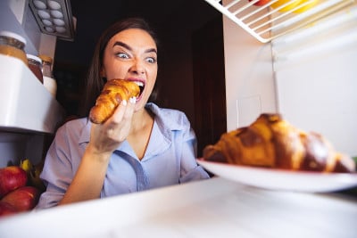 饥饿的女人从冰箱里吃牛角面包，从里面看