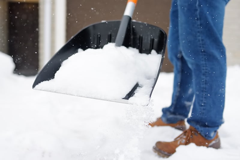 一名成熟的男子在暴风雪中清理房子附近的积雪。有人在铲车道上的雪。巨大的雪堆中。一场暴风雪过后，这个城