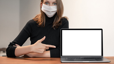 美丽的白人妇女的肖像戴着医疗保护面罩室内。概念与模板模型的空白屏幕上的笔记本电脑