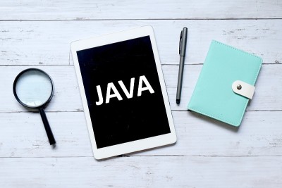 俯视图放大镜，钢笔，笔记本和平板电脑写的“JAVA”在白色的木制背景。