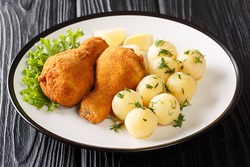 维也纳风味Backhendl面包屑炸鸡腿与柠檬和新土豆近在盘子。水平