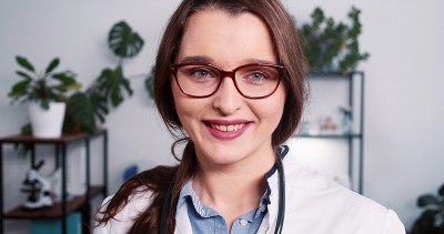 特写年轻美丽的白种人女医生穿白大褂，眼镜摆姿势在轻诊所办公室。