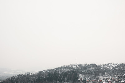 极简主义的视野，大量的负空间，被雪覆盖的岩石山，顶部有树木和电视天线，上升在一小群房子之上