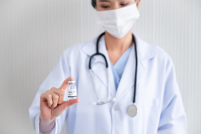 一名戴着口罩的女医生站在实验室里，手里拿着一瓶保护冠状病毒的疫苗。预防COVID-19传播的概念。