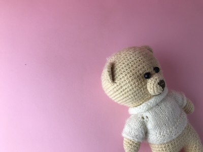 室内玩具-一个柔软的针织熊在粉红色背景的角落里。熊由天然材料，钩针线。可爱的礼物