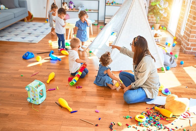 美丽的老师和一群蹒跚学步的孩子在幼儿园玩很多玩具