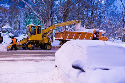 抓斗装载机清除道路上的积雪。一辆扫雪机把雪倒进卡车里。