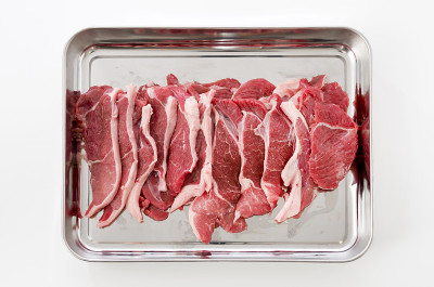 不锈钢托盘上的生羊肉，白色背景。