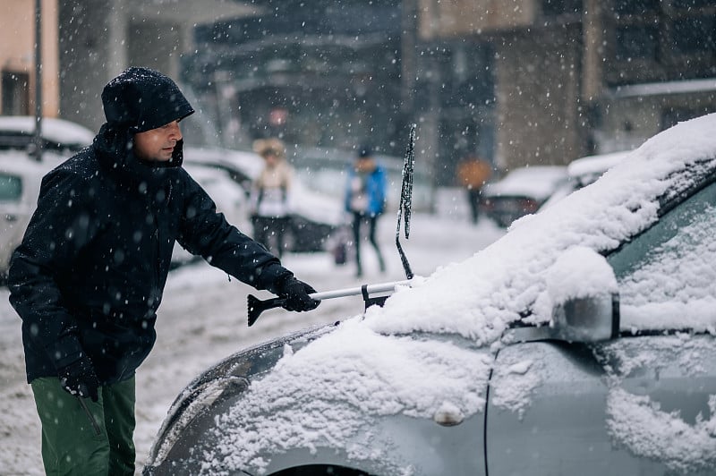 中年男子正在清理汽车上的冰雪