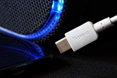 白色usb type-c连接器旁边的深色智能手机和蓝色LED灯在黑色背景。现代技术和数据传输的概念。