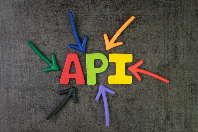 API，应用程序编程接口概念，多色箭头指向字API在黑色水泥黑板墙的中心，桥梁连接和发送应用程序之间