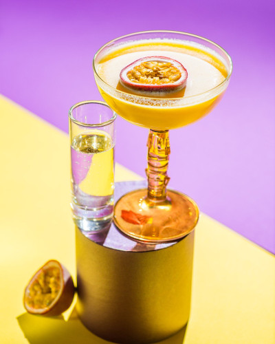 黄色的热带鸡尾酒配上百香果，以热带植物的叶子和遮阳伞为背景拍摄。颜色背景