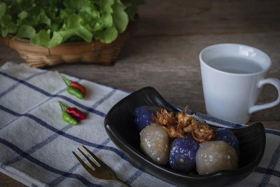 西米猪肉在黑色的盘子里，炸蒜头有辣椒，左手和生菜篮子，白色的杯子放在后面，金色的叉子放在前面的桌布和