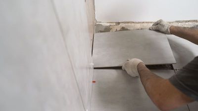 瓷砖师傅把灰色瓷砖粘在墙上。工匠把瓷砖粘在浴室的墙上
