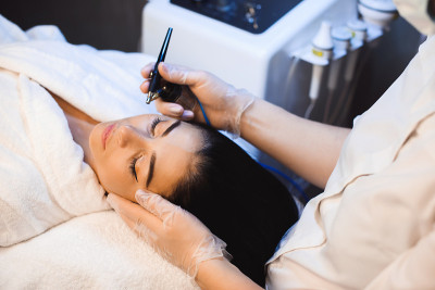 上视图照片的脸部治疗与现代仪器在迷人的白人女士的脸在水疗沙龙