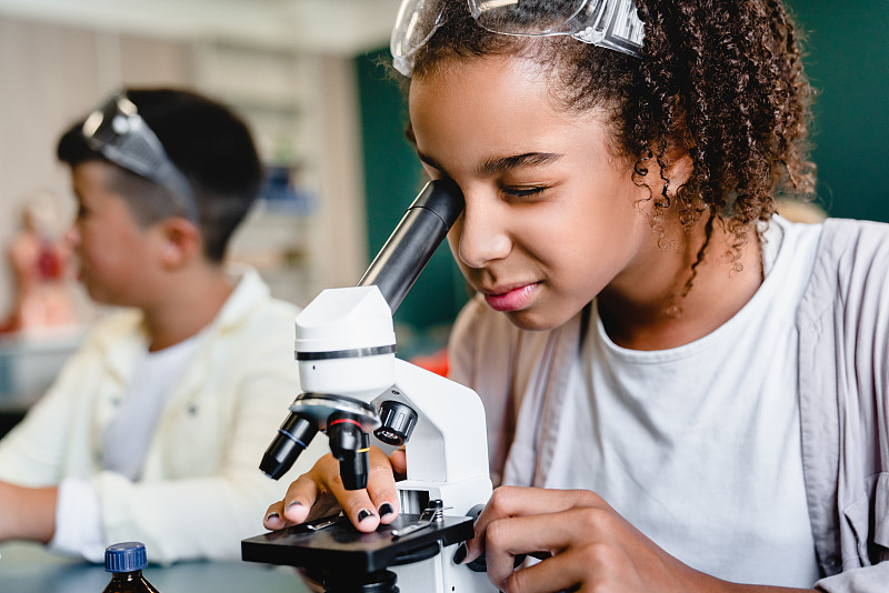 非裔美国女学生在学校实验室的生物化学课上使用显微镜。科学课的概念