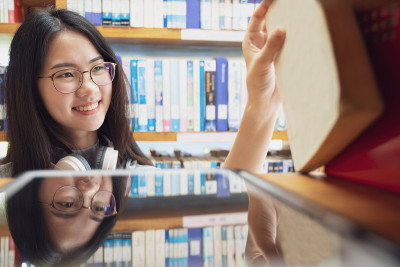 回到学校教育知识学院的大学理念，美丽的女大学生抱着她的书微笑着站在图书馆，学习和教育的理念