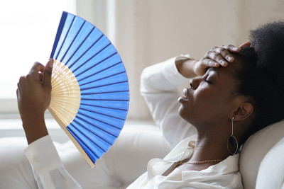 一位非洲裔女商人正坐在家里的客厅里挥动扇子，中暑