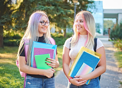 年轻开朗的女学生用五颜六色的头发站在大学校园，拿着小册子和背包-回到学校的人的生活理念与两个模型
