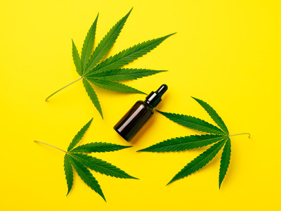 滴瓶中的大麻油，黄色背景下的绿叶。替代医学概念。