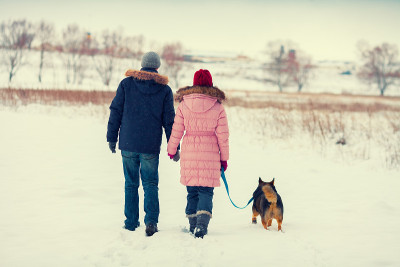 一对年轻夫妇带着狗在雪地里散步
